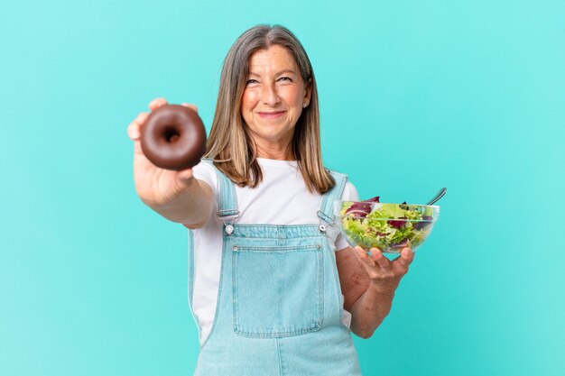 hübsche frau mittleren alters mit einem donut und einem salat. Diätkonzept