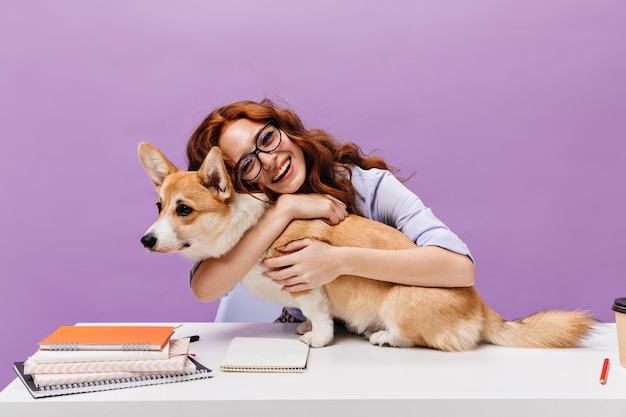 Hübsche Frau umarmt Corgi und posiert im Büro