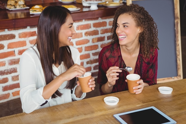 Hübsche Freundinnen, die einen Kaffee unter Verwendung des Tabletten-PC genießen