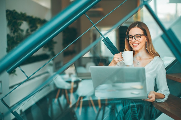 Hübsche Geschäftsfrau, die oh die Bürotreppe sitzt, Kaffeepause hat und Netz-surfendes Internet