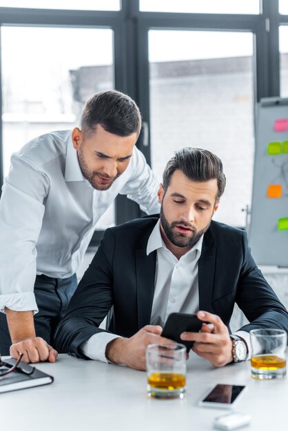 Hübsche Geschäftsleute, die im modernen Büro auf Smartphone schauen