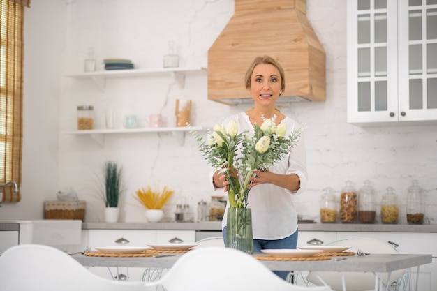 Hübsche Hausfrau, die schöne Blumen in die Vase setzt