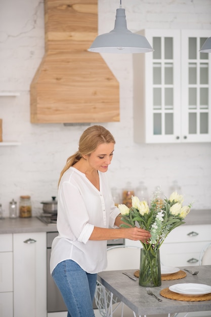 Hübsche Hausfrau, die weiße Blumen in die Vase setzt