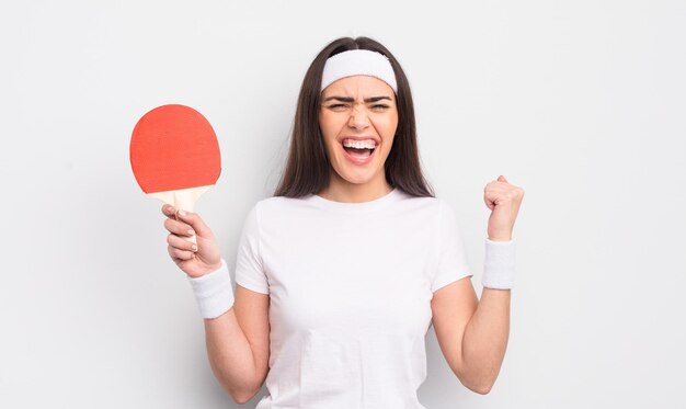 Hübsche hispanische Frau, die aggressiv mit einem wütenden Ausdruck schreit. Ping-Pong-Konzept