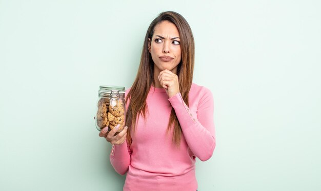 Hübsche hispanische Frau, die denkt, sich zweifelhaft und verwirrt fühlt. Cookies-Konzept