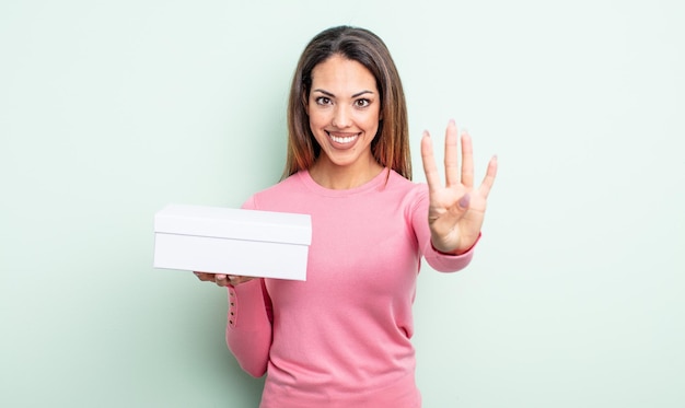 Hübsche hispanische Frau, die freundlich lächelt und aussieht und Nummer vier zeigt. White-Box-Verpackungskonzept