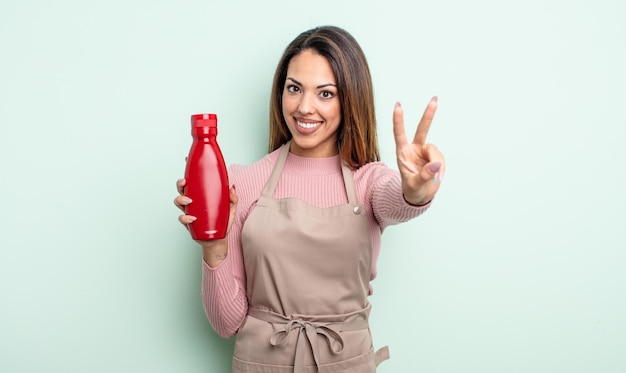 Hübsche hispanische Frau, die glücklich lächelt und schaut und Sieg oder Frieden gestikuliert. Ketchup-Konzept