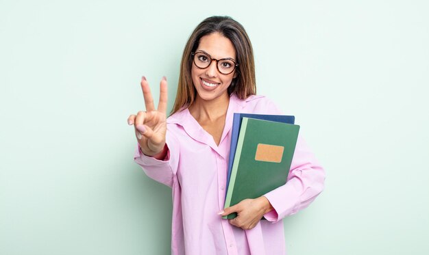 Hübsche hispanische Frau, die glücklich lächelt und schaut und Sieg oder Frieden gestikuliert. Notebook-Konzept