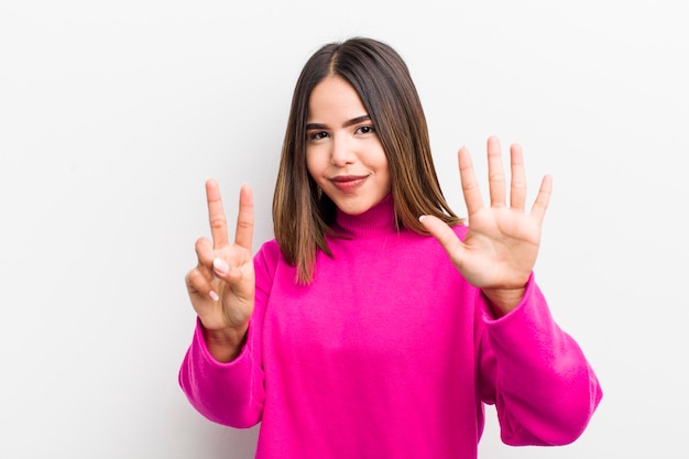 Hübsche hispanische Frau, die lächelt und freundlich aussieht und die Nummer sieben oder siebte zeigt, wobei die Hand nach unten zählt