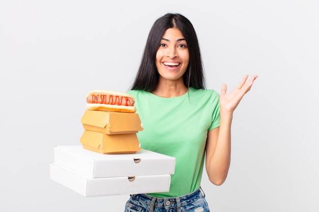 Hübsche hispanische Frau, die sich glücklich fühlt, überrascht, eine Lösung oder Idee zu verwirklichen und Fast-Food-Boxen zum Mitnehmen zu halten