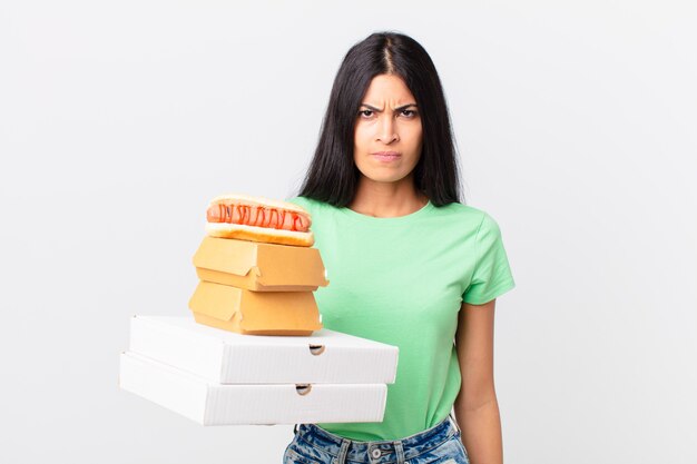 Hübsche hispanische Frau, die sich verwirrt und verwirrt fühlt und Fast-Food-Boxen zum Mitnehmen hält?