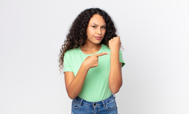 Hübsche hispanische Frau, die ungeduldig und wütend aussieht, auf die Uhr zeigt, um Pünktlichkeit bittet, will pünktlich sein