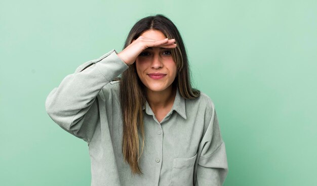 Foto hübsche hispanische frau, die verwirrt und erstaunt aussieht, mit der hand über der stirn, die weit weg schaut und zuschaut oder sucht