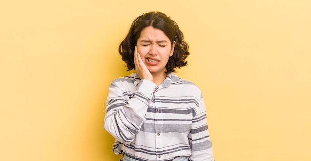 Hübsche hispanische Frau, die Wange hält und unter schmerzhaften Zahnschmerzen leidet, fühlt sich krank, elend und unglücklich auf der Suche nach einem Zahnarzt