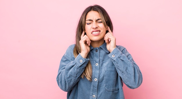 Hübsche hispanische Frau, die wütend, gestresst und genervt aussieht und beide Ohren zu einem ohrenbetäubenden Geräusch oder lauter Musik bedeckt