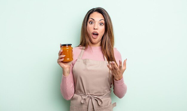 Hübsche hispanische Frau erstaunt, schockiert und erstaunt mit einer unglaublichen Überraschung. Pfirsichmarmelade Konzept