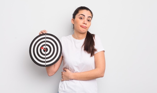 Hübsche hispanische frau zuckt mit den achseln, fühlt sich verwirrt und unsicher. darts zielkonzept