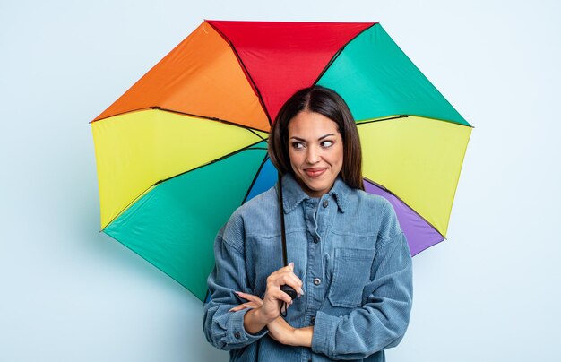 Hübsche hispanische Frau zuckt mit den Schultern, fühlt sich verwirrt und unsicher. Regenschirmkonzept