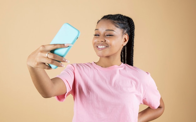 Hübsche junge Afrikanerin, die mit ihrem beigefarbenen Hintergrund des Smartphones selfie macht