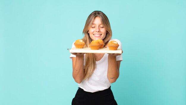 Hübsche junge blonde Frau mit einem Muffins-Tablett