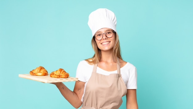 Hübsche junge blonde Kochfrau, die ein Tablett mit Croissants hält