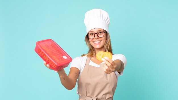 Hübsche junge blonde Kochfrau und hält eine Tupperware