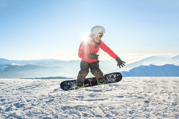 Hübsche junge Frau auf dem Snowboard, das über den Hang springt