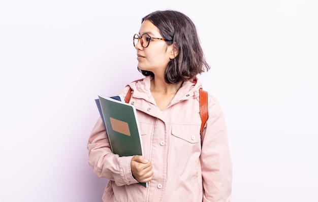 Hübsche junge Frau auf der Profilansicht, die denkt, sich vorstellt oder träumt. Student mit Bücherkonzept