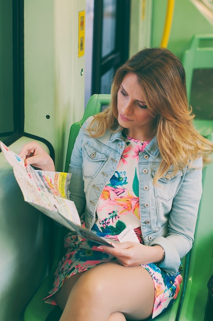 Hübsche junge Frau auf einer Straßenbahn / Straßenbahn, die eine Karte schaut, während ihrer touristischen Reise