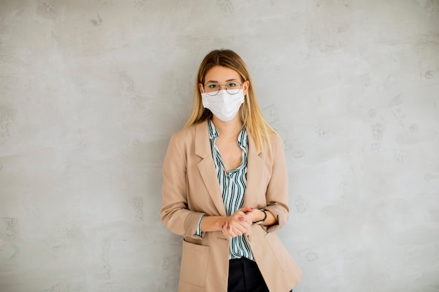 Foto hübsche junge frau, die an der grauen wand steht und eine atemmaske von coronavirus-krankheit trägt