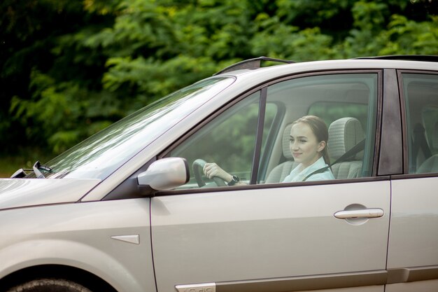 Hübsche, junge Frau, die ein Auto fährt - Einladung zum Reisen. Mietwagen oder Urlaub.