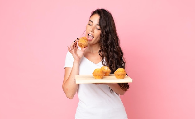 Hübsche junge Frau, die ein Muffinsblech hält