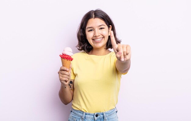 Hübsche junge Frau, die freundlich lächelt und aussieht und Nummer eins zeigt. Eiskonzept