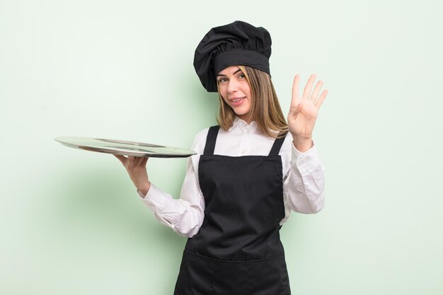 Hübsche junge Frau, die freundlich lächelt und aussieht und Nummer vier zeigt. Koch mit Tablettkonzept