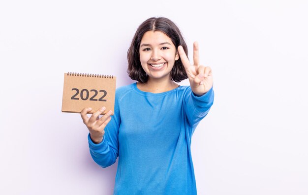 Hübsche junge Frau, die freundlich lächelt und aussieht und Nummer zwei zeigt. Kalenderkonzept 2022