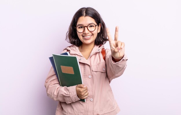 Hübsche junge Frau, die freundlich lächelt und aussieht und Nummer zwei zeigt. Student mit Bücherkonzept