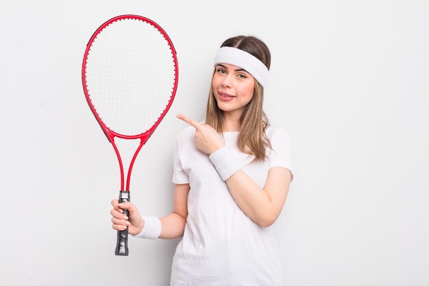 Hübsche junge Frau, die fröhlich lächelt, sich glücklich fühlt und zur Seite zeigt. Tennis-Konzept