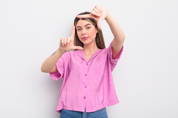 Hübsche junge Frau, die glücklich, freundlich und positiv lächelt und ein Porträt oder einen Fotorahmen mit den Händen macht