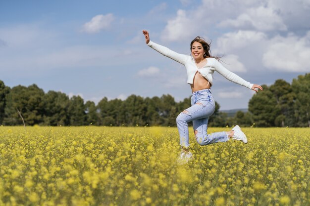 Hübsche junge Frau, die glücklich in ein Feld von gelben Blumen springt