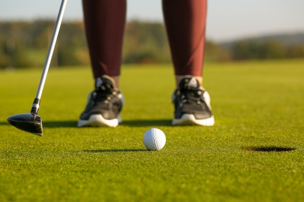 Hübsche junge Frau, die Golf auf Übungsplatz spielt, schlägt den Golfball in das Loch, Sportkonzept