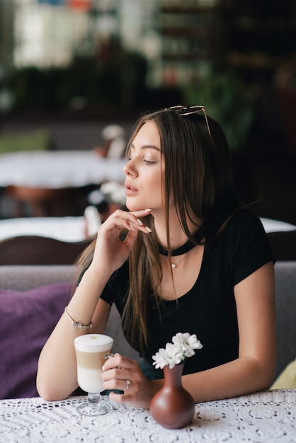Hübsche junge Frau, die in einem Café mit einer Tasse Kaffee Latte sitzt.