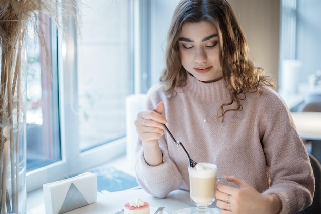 Hübsche junge Frau, die mit einer Tasse Cappuccino im Café sitzt