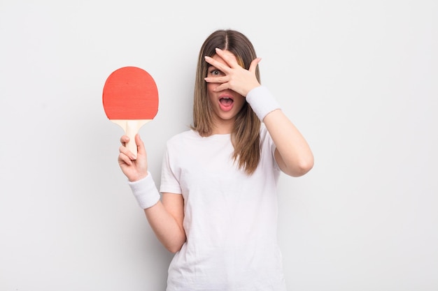 Hübsche junge Frau, die schockiert, verängstigt oder verängstigt aussieht und das Gesicht mit Hand-Ping-Pong-Konzept bedeckt