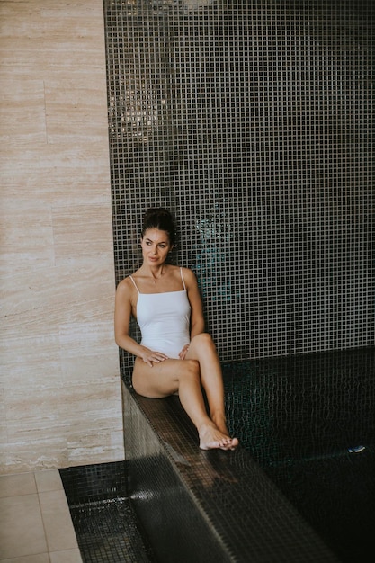 Hübsche junge Frau, die sich am Pool des Hallenbades entspannt