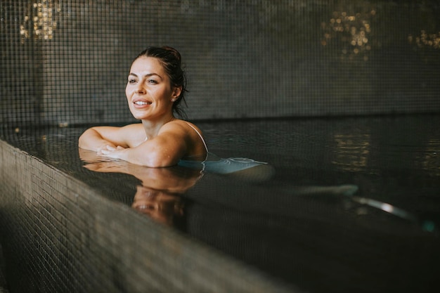 Hübsche junge Frau, die sich am Pool des Hallenbades entspannt