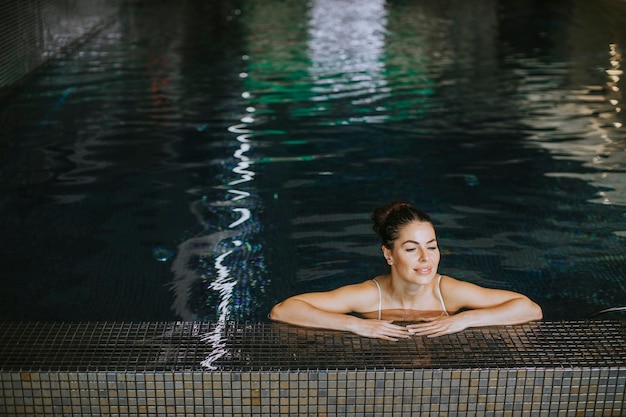 Hübsche junge Frau, die sich am Pool des Hallenbades entspannt