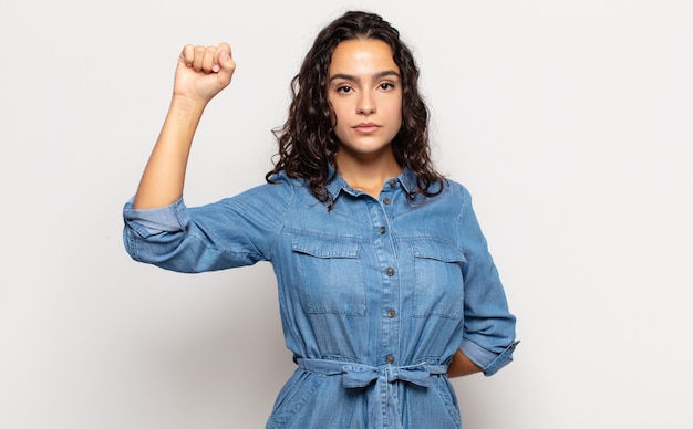 Hübsche junge Frau, die sich ernst, stark und rebellisch fühlt, die Faust erhebt, protestiert oder für die Revolution kämpft