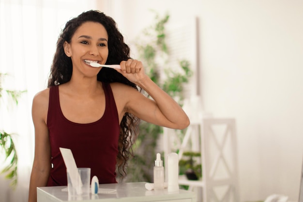 Hübsche junge Frau, die Zähne mit Zahnpasta in der Nähe des Spiegels zu Hause putzt
