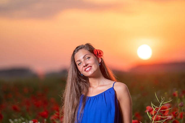 Hübsche junge Frau im Mohnfeld mit Sonnenuntergang Landschaft im Hintergrund warmes Sonnenunterganglicht
