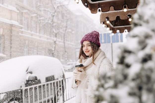 Hübsche junge Frau im Winteroutfit, die während des Schneefalls geht